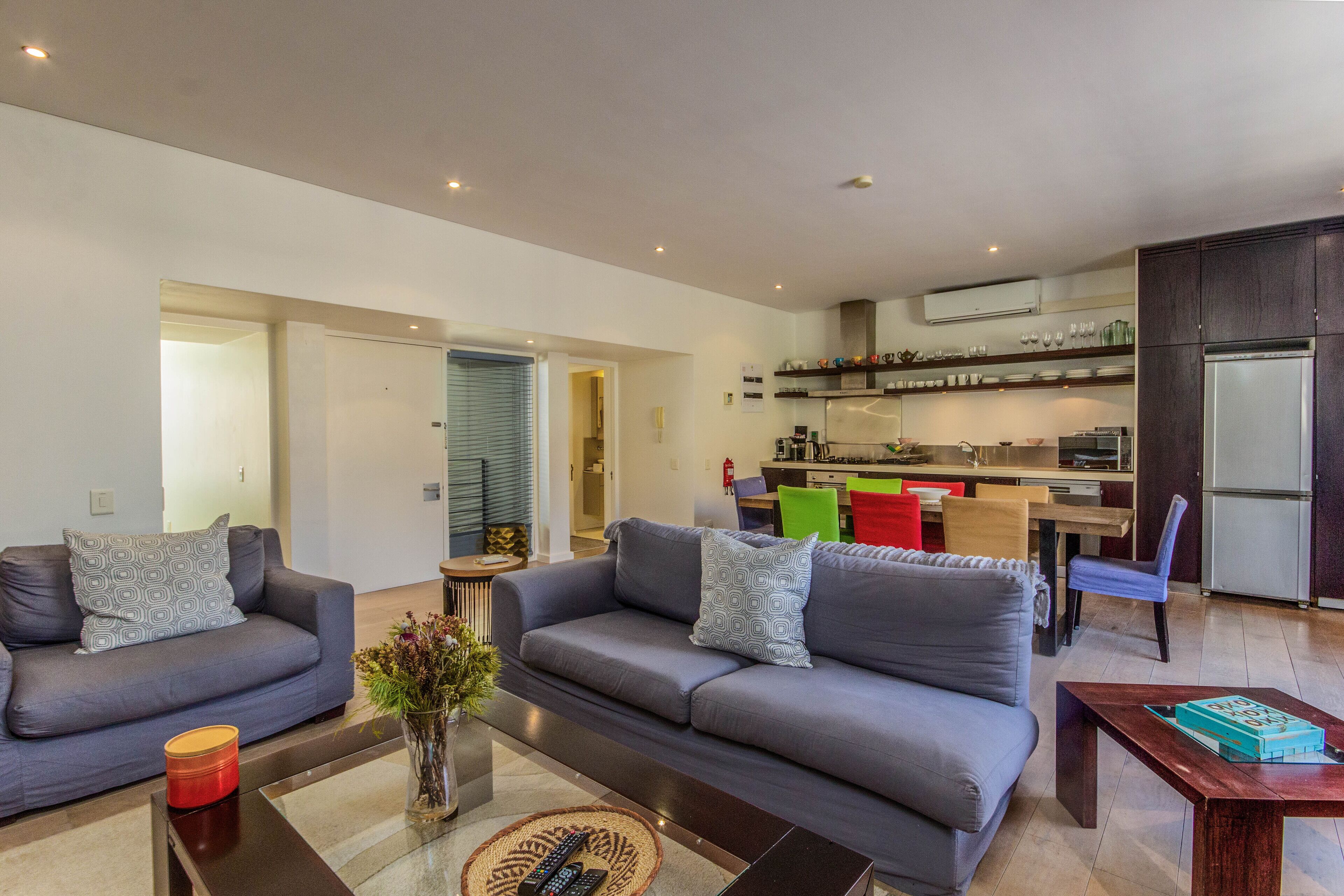 A modern living room with a grey sofa, a coffee table, and a kitchen area in the background.