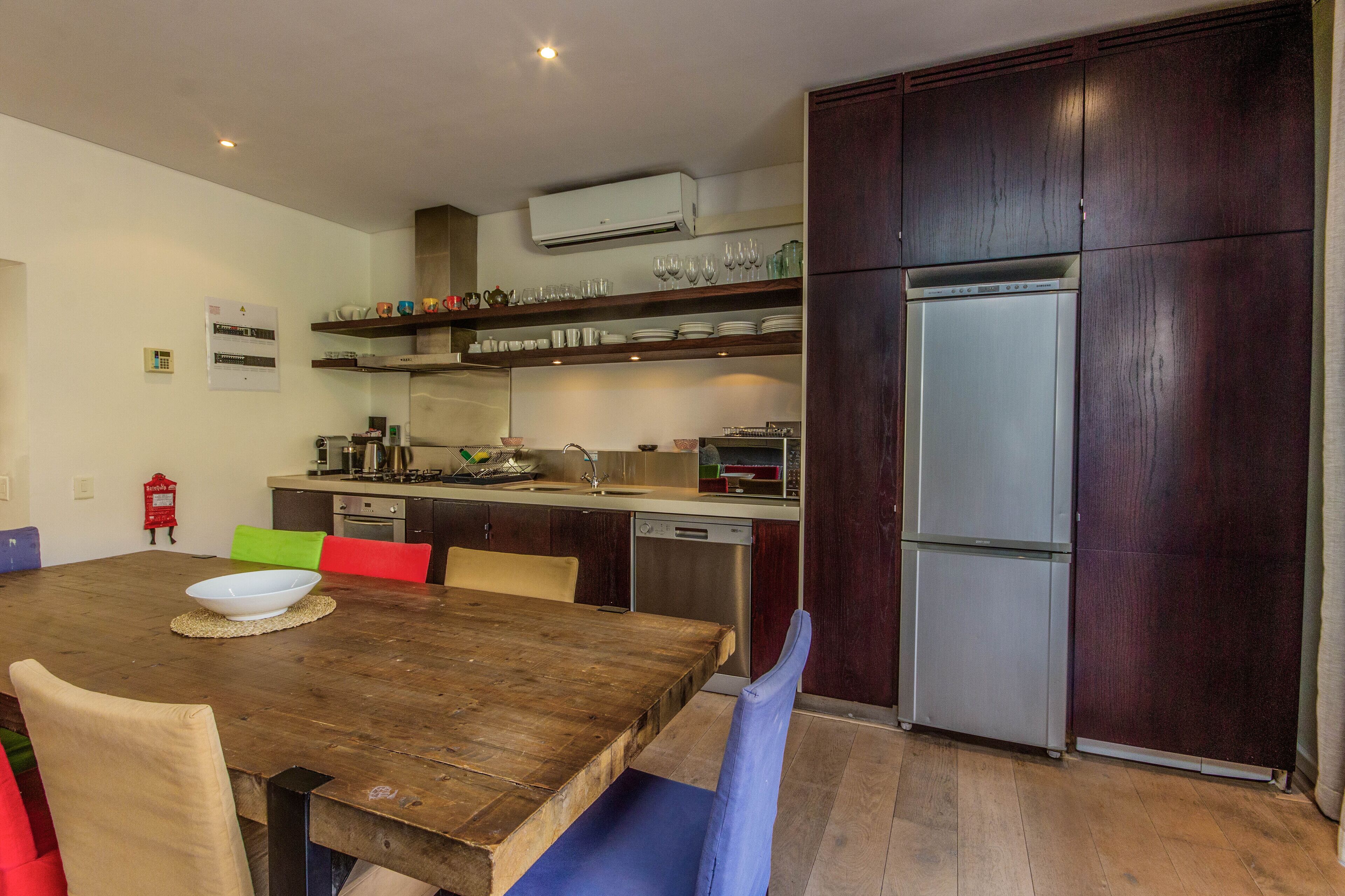 A modern kitchen with a wooden dining table, chairs, a built-in oven, a dishwasher, and a refrigerator.