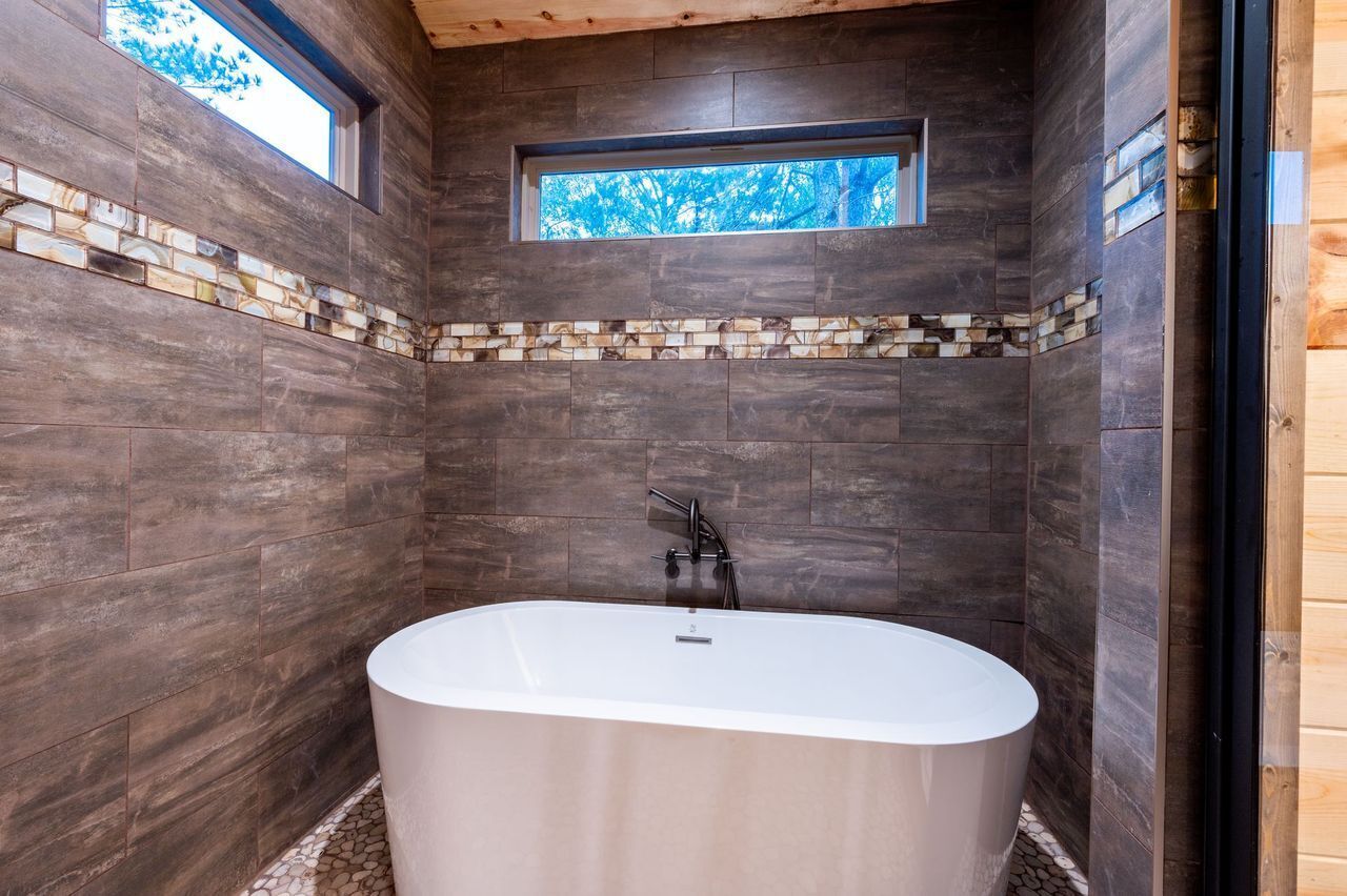 A modern bathroom with dark wooden walls, a white bathtub, and a small window.