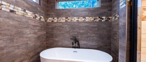 A modern bathroom with dark wooden walls, a white bathtub, and a small window.