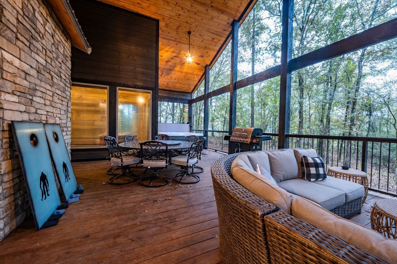 A wooden deck with a dining table and chairs, a wicker sofa, and a grill.