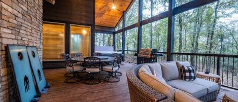 A wooden deck with a dining table and chairs, a wicker sofa, and a grill.
