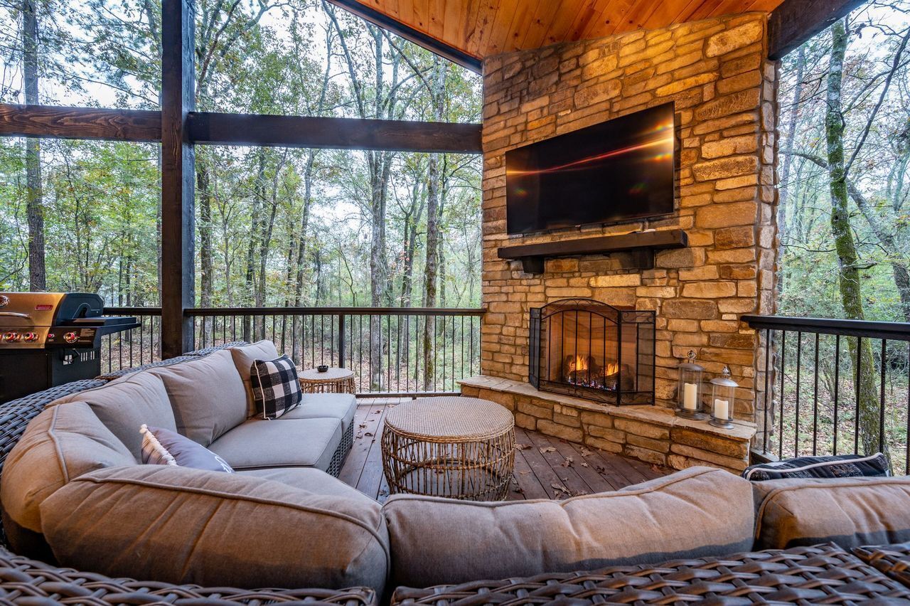 A cozy outdoor seating area with a stone fireplace, a flat-screen TV, and a grill.