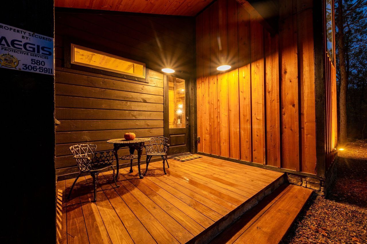 Una cabaña de madera con un porche, dos sillas, una mesa y una ventana iluminada.