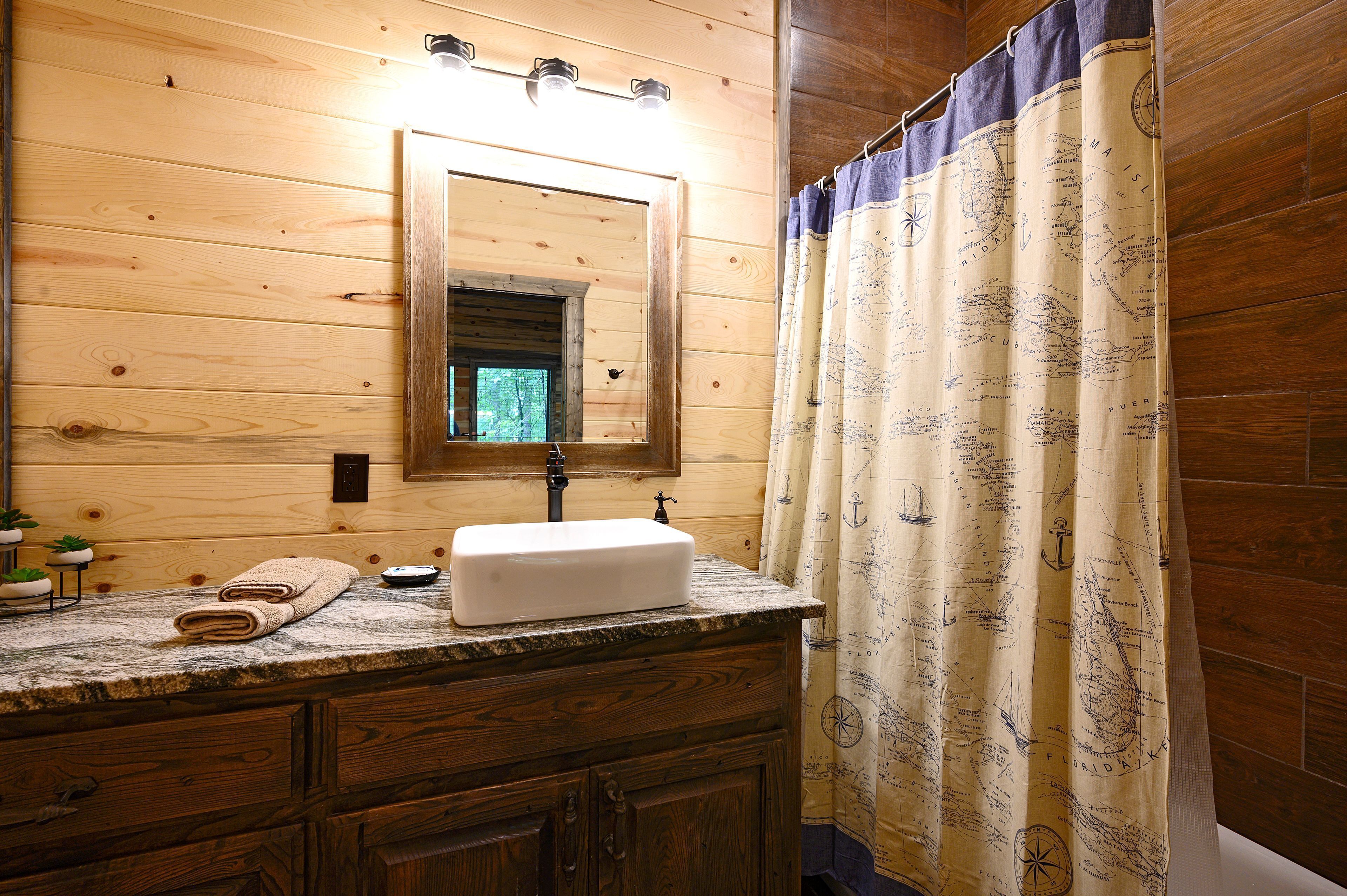 Un baño de cabaña de madera con tocador de madera, un lavamanos y un espejo encima.