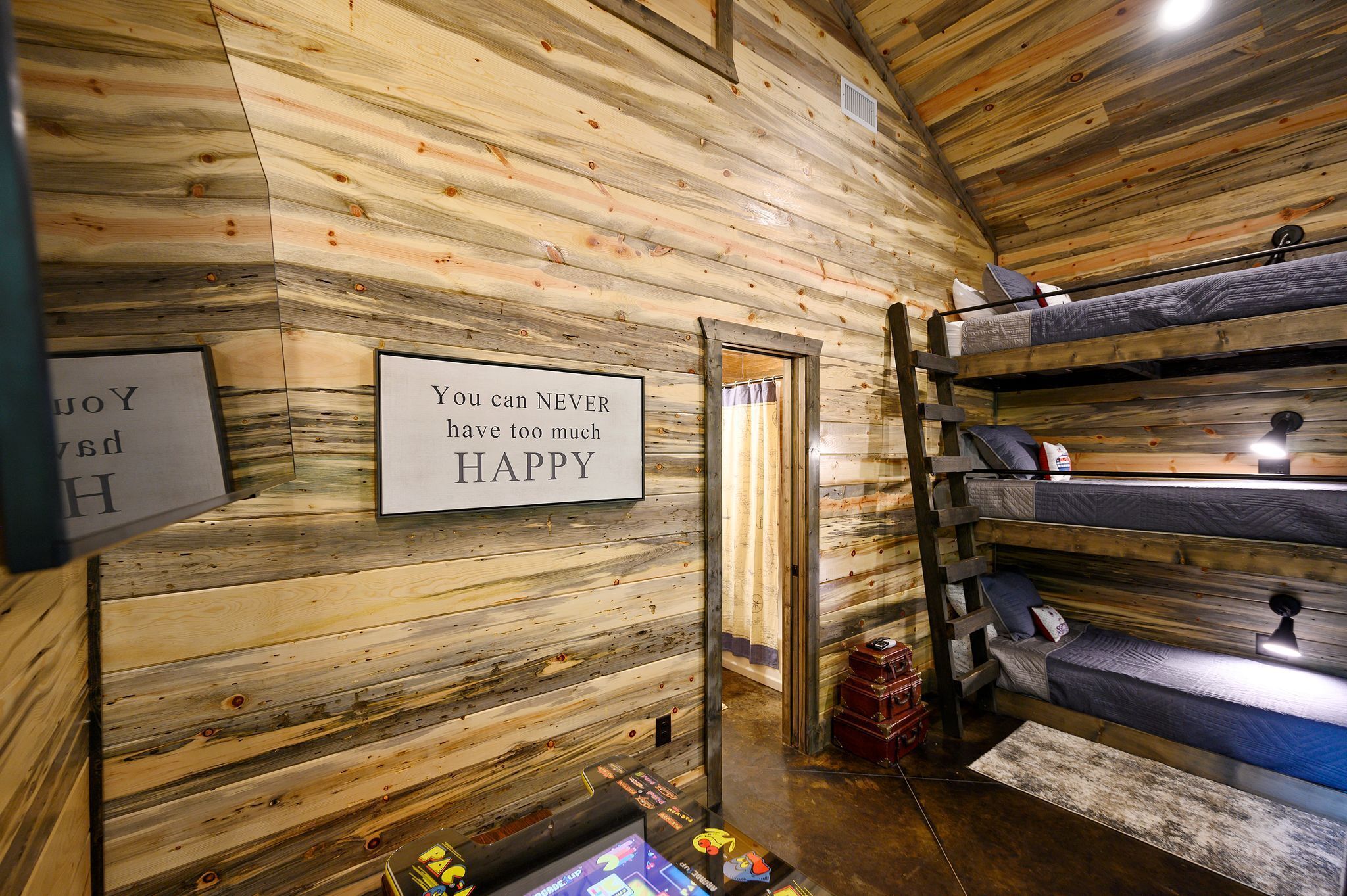 A rustic cabin interior with wooden walls, bunk beds, a ladder, a sign, and a suitcase.