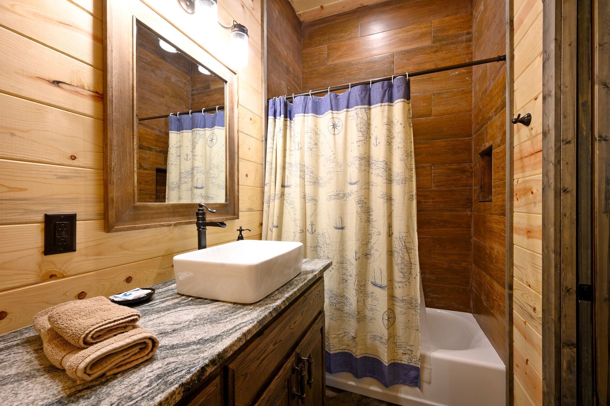 Une salle de bain rustique, avec une cabine en bois, un lavabo, un miroir et une baignoire.