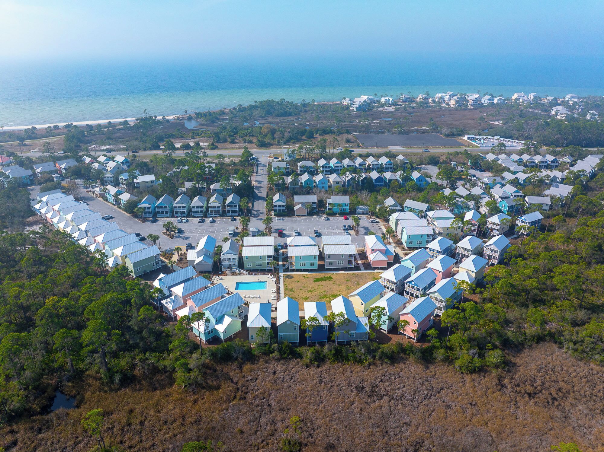 Vue aérienne d’une station balnéaire dont l’aménagement a la forme d’un cœur, avec une piscine centrale, plusieurs bâtiments de style bungalow et une plage.