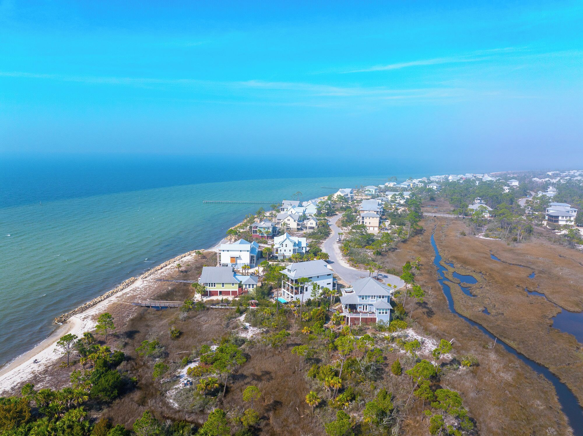 A coastal residential area with houses along the beachfront, a clear view of the ocean, and a network of roads connecting the properties.