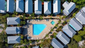 An aerial view of a resort with multiple buildings, a central swimming pool, and surrounding lounge areas.