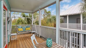 A covered porch with a wooden table, a white chair, and a bench with cushions.