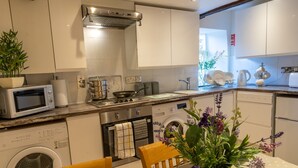 A modern kitchen with a microwave, stove, oven, and washing machine. There is a dining table with chairs and a vase of flowers. - Highgate View Apartment -   Kendal Town Centre (Kendal)