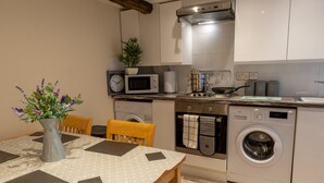 A modern kitchen with a dining area, including a table with a vase of flowers, a microwave, a stove, and a washing machine. - Highgate View Apartment -   Kendal Town Centre (Kendal)