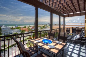 Een balkon met een eettafel, met uitzicht op een strand en stadsgezicht.