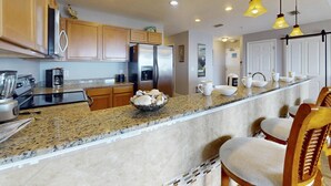 A kitchen with granite countertops, wooden cabinets, stainless steel appliances, and bar stools. - Top Floor Waterfront Resort. Steps to the Beach,Pool, Hot Tub, Dock, Great View +Tickets to Fun! (Treasure Island)