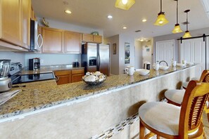 A kitchen with granite countertops, wooden cabinets, stainless steel appliances, and bar stools.