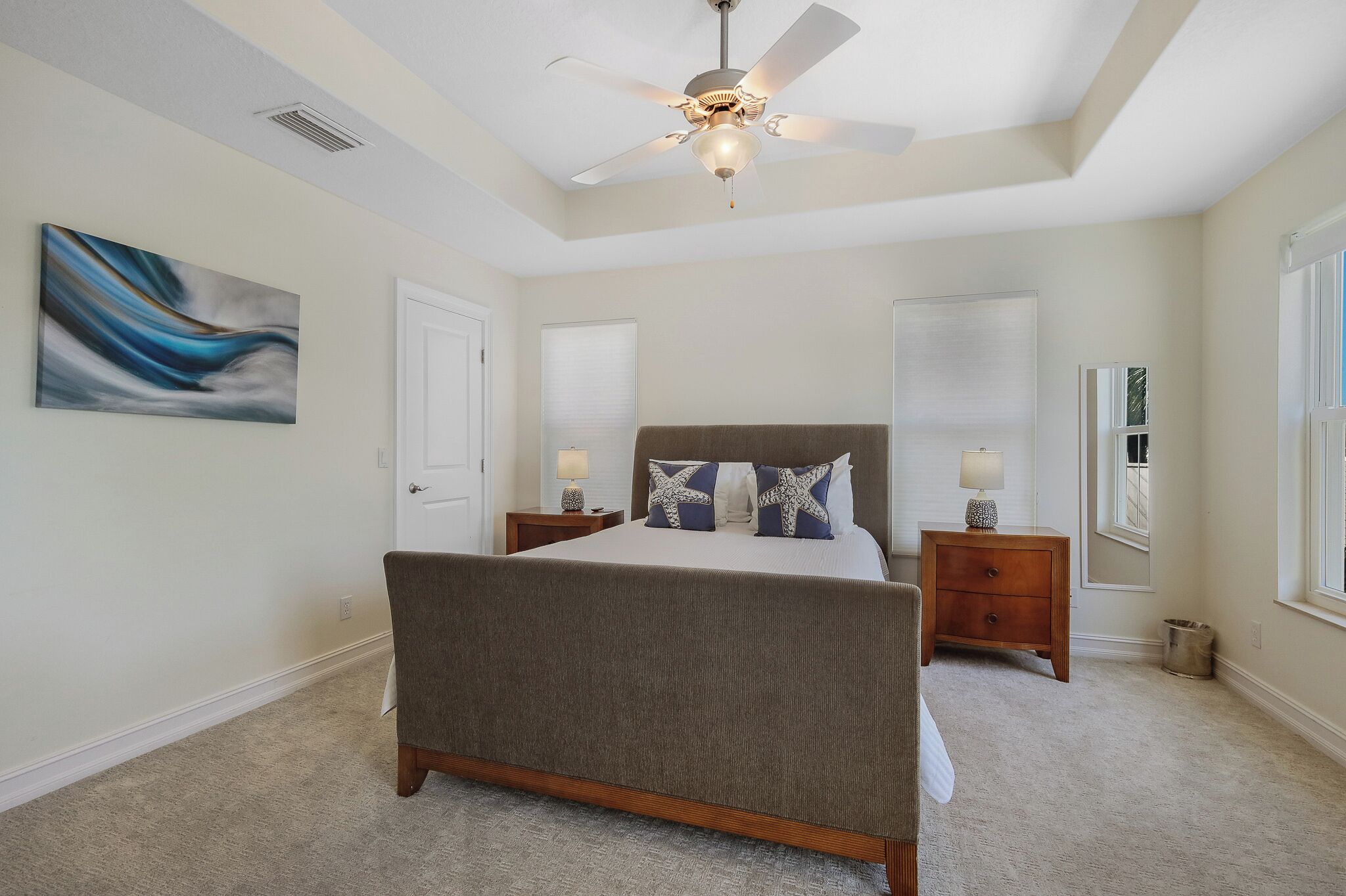 A bedroom with a bed, nightstands, a ceiling fan, and a painting on the wall.