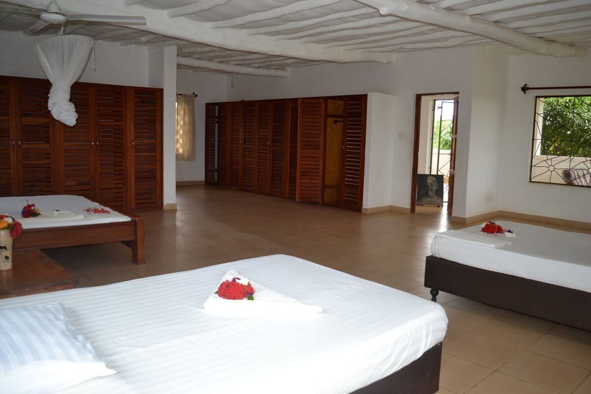 A hotel room with two beds, wooden wardrobes, a ceiling fan, and a window with a view of greenery.