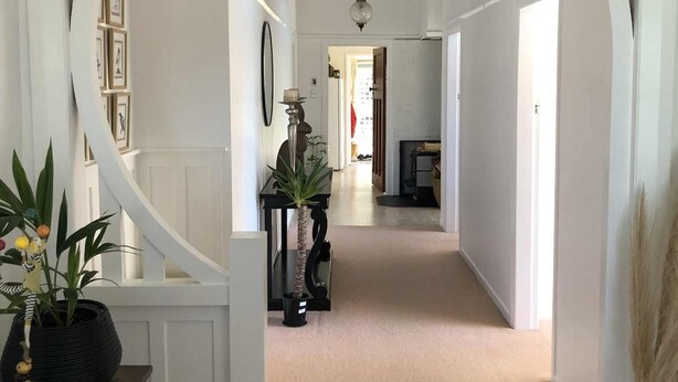 A hallway with white walls and a curved archway. There are framed pictures on the wall, a ceiling fan, and a floor lamp.