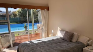 A bedroom with a large bed, a nightstand, a lamp, and a view of a swimming pool through a glass door.