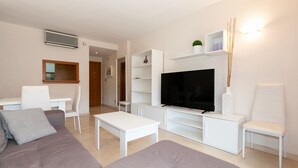 A modern living room with a flat-screen TV, white furniture, and a minimalist design. - AirCon Apartment with Pool on the rooftop · UHC CENTRAL PARK 327 (Salou)