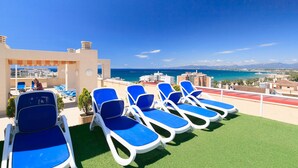 A rooftop lounge area with blue lounge chairs and a view of the sea and buildings. - AirCon Apartment with Pool on the rooftop · UHC CENTRAL PARK 327 (Salou)