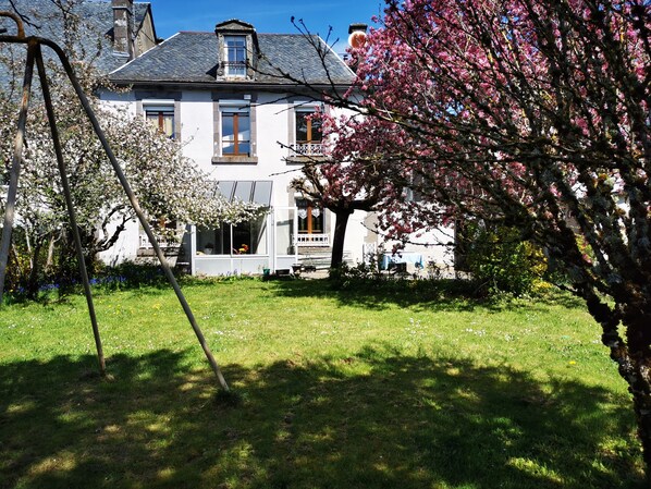 A two-story house with a visible balcony and a garden in front.