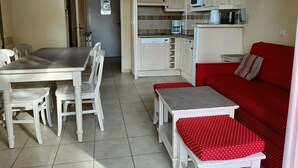 Une cuisine compacte avec un coin repas, un canapé rouge et une petite table agrémentée d’un coussin rouge.