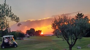 Un parcours de golf avec un chariot de golf, des arbres et un coucher de soleil en arrière-plan.