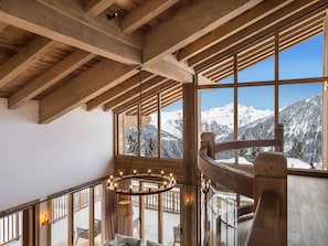 A wooden interior with a staircase, large windows with a snowy mountain view, and a hanging light fixture.