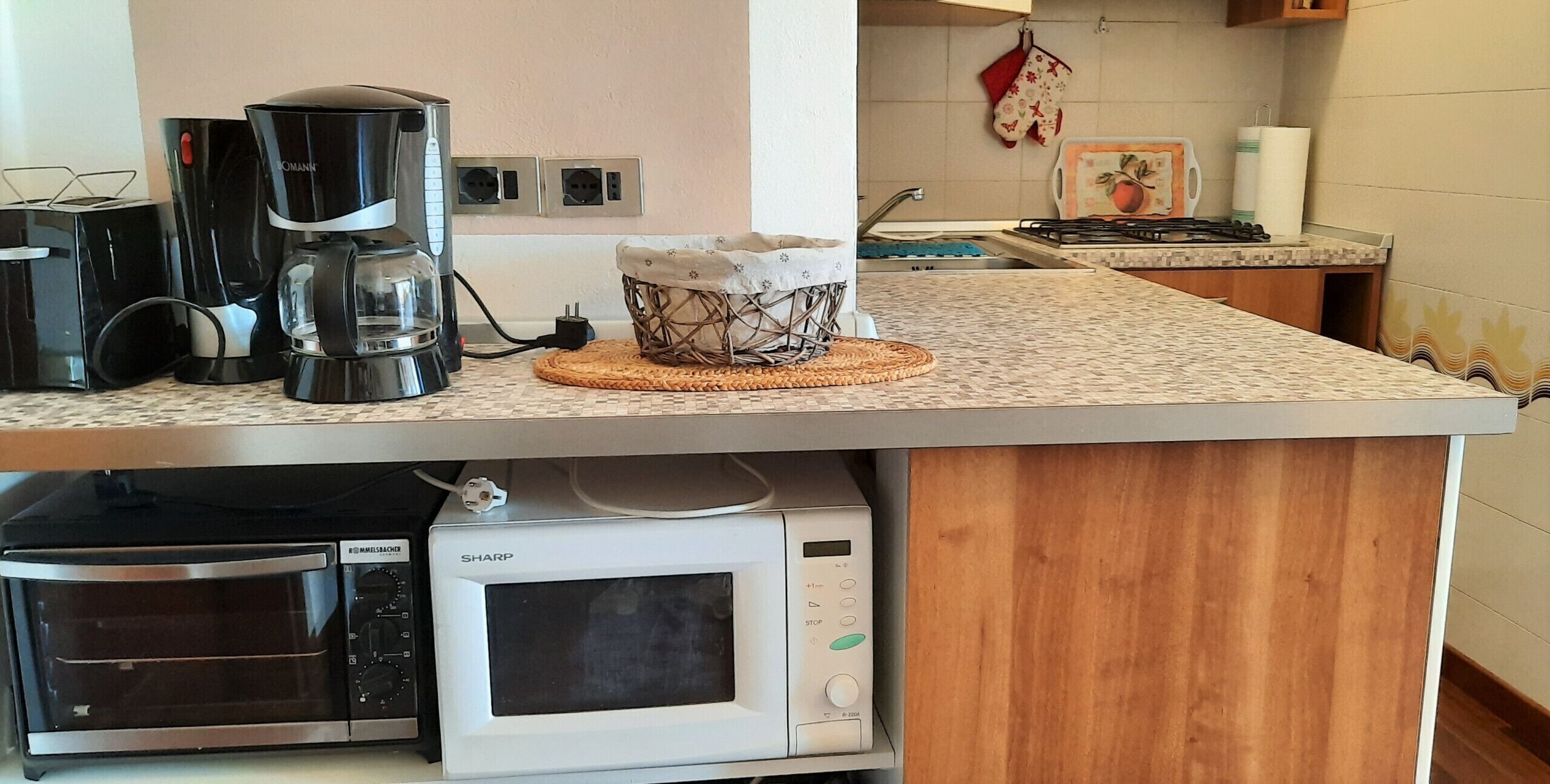A kitchen with a coffee maker, microwave, oven, and a basket on the countertop.