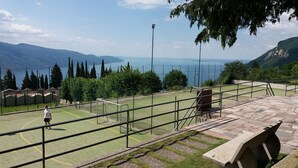 A tennis court with a net, surrounded by a stone wall and a view of a lake and mountains. - Appartamento Tobias 201 La Portella (Tignale)