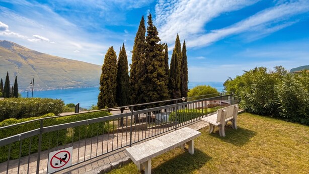 A park with a bench, a no-pet sign, and a view of a lake. - Appartamento Tobias 201 La Portella (Tignale)