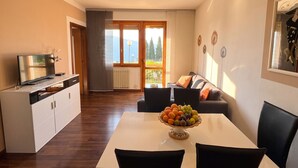 A modern living room with a sofa, a dining table with chairs, a TV, and a view of the outdoors. - Appartamento Tobias 201 La Portella (Tignale)