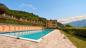 A swimming pool with stone tiles, a stone pathway, and a building with balconies on a hillside. - Appartamento Tobias 201 La Portella (Tignale)