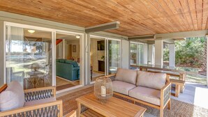 Un espace de vie à aire ouverte avec un plafond en bois, des portes-fenêtres coulissantes donnant sur un patio et un canapé placé face à une cheminée.