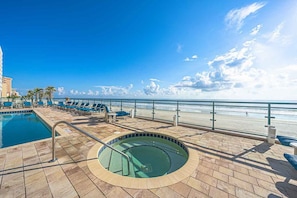 A pool area with a hot tub, lounge chairs, and a view of the beach.