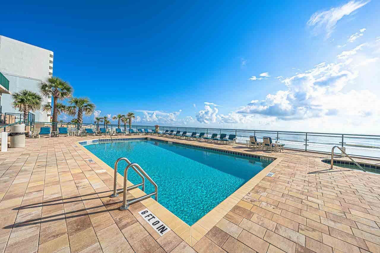 A pool area with a clear blue pool, lounge chairs, and a view of the ocean.
