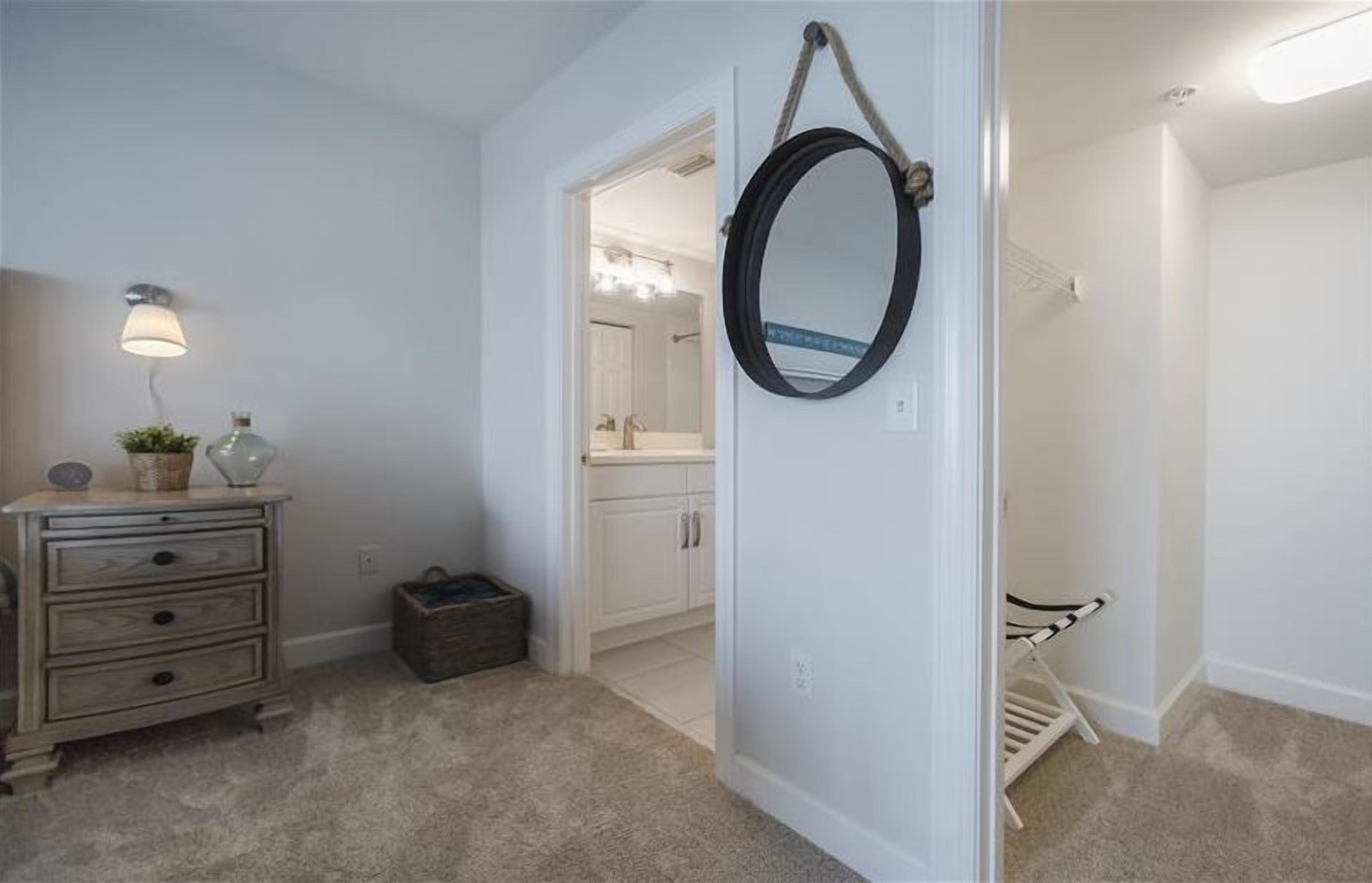 A bedroom with a dresser, a lamp, a mirror, and a walk-in closet.