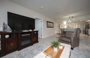 En moderne stue med et fladskærms-tv, en underholdningsenhed i mørkt træ, en lædersofa og et træsofa bord med en plante.