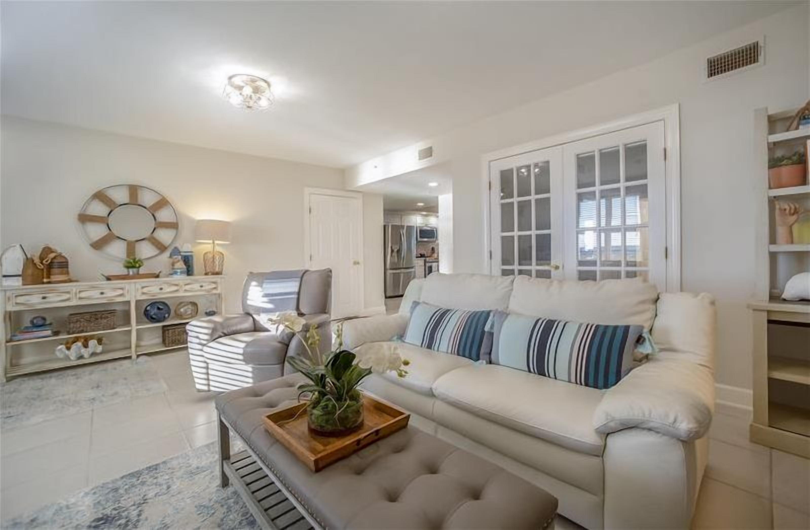 A modern living room with a white sofa, a coffee table with a tray and plant, a sideboard, and a large mirror.