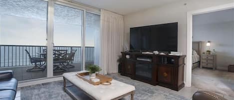A living room with a large TV, a ceiling fan, a sliding glass door to a balcony, and a wooden coffee table.