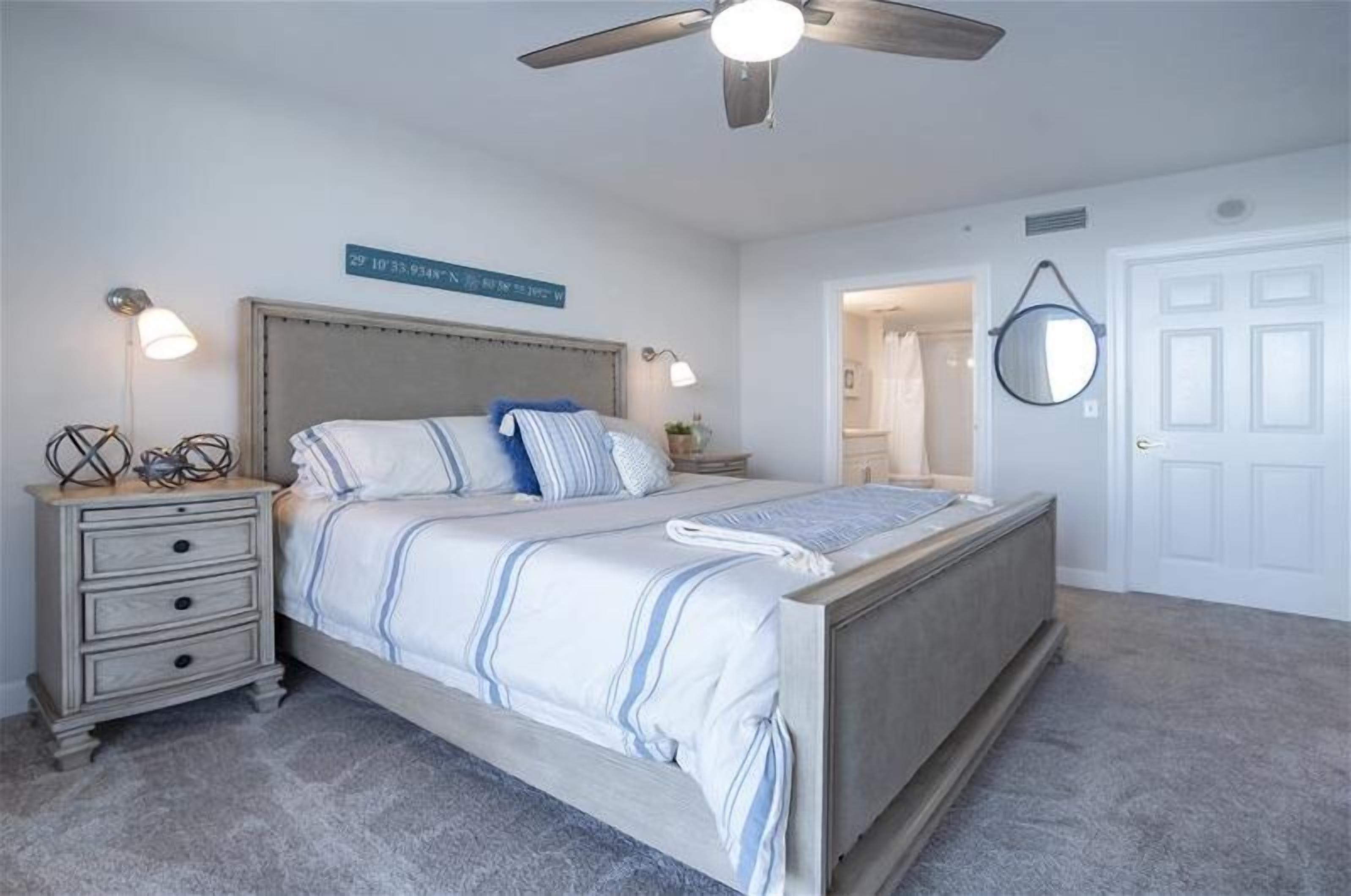 Ein Schlafzimmer mit Bett, Nachttischen, Deckenventilator und einer Tür.
