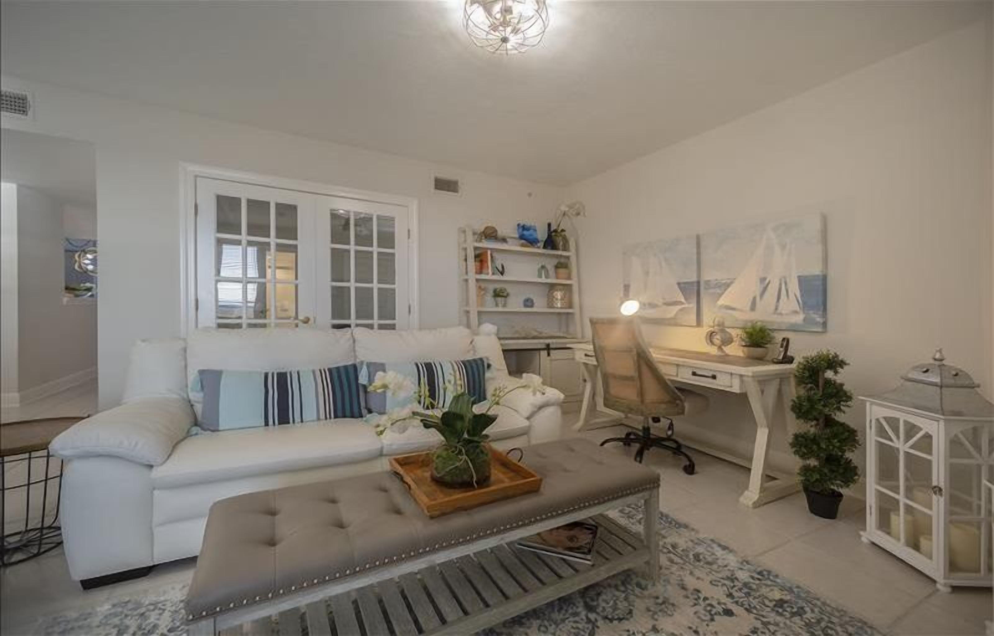 Una sala de estar con un sofá blanco, una mesa de centro de madera, un escritorio y una estantería.