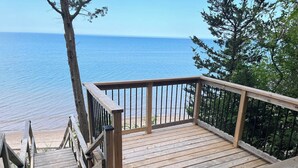 Eine Holzterrasse mit Geländer, die auf einen Strand und das Meer blickt.
