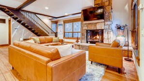 Ein großzügiges Wohnzimmer mit Kamin aus Stein, Ledersofas und einer Holztreppe.