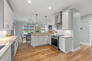 A modern kitchen with white cabinets, a wooden floor, and pendant lighting.