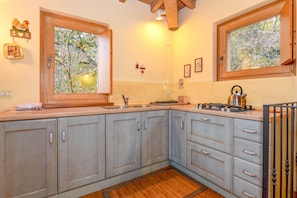 Una cocina con armarios de madera, una ventana con vista a árboles, un hervidor en la estufa y un piso de madera.