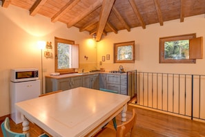 Una cocina con vigas de madera, una mesa blanca, un microondas y una ventana con vistas a árboles.