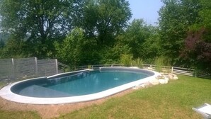 Une piscine à bord incurvé, entourée d’une clôture blanche et d’une végétation luxuriante.